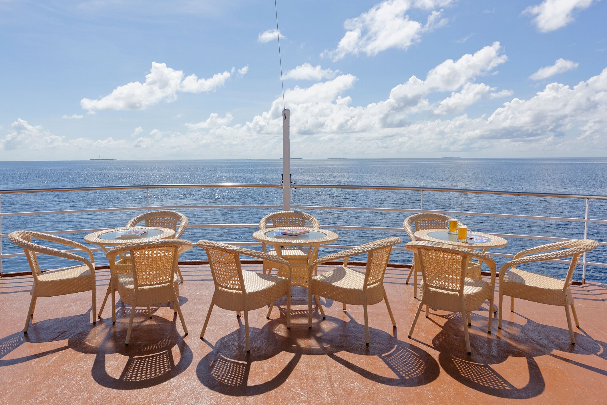 Un terrazzino con sedie in vimini e un tavolo rotondo, con vista su un mare calmo e un'isola in lontananza.