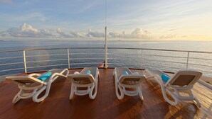 A deck with four white lounge chairs, each with a blue cushion, overlooking a calm sea with a clear sky. - Yasawa Princess (Malé)