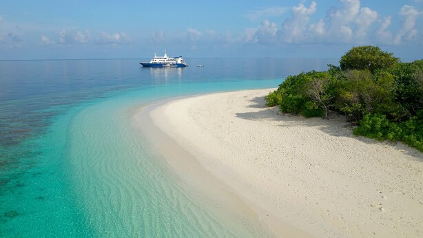 A beach with clear turquoise waters and a boat in the distance. - Yasawa Princess (Malé)