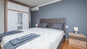 Un dormitorio con una cama grande, un armario, una mesita de noche con lámpara y un equipo de aire acondicionado en la pared.