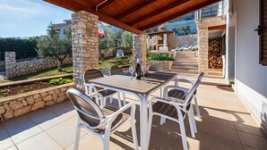 Un espacio comedor al aire libre con techo, pilares de piedra, una mesa y sillas.