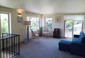 A living room with a blue sofa, a white chair, a floor lamp, and a small table with a plant. - Villa Calabria (Seattle)