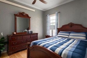 Un dormitorio con una cama de madera, un aparador, un espejo y un ventilador de techo.