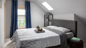 Makuuhuoneessa on sänky, yöpöytä, ikkuna verhoilla, kattovalaisin ja pieni kasvi hyllyllä.