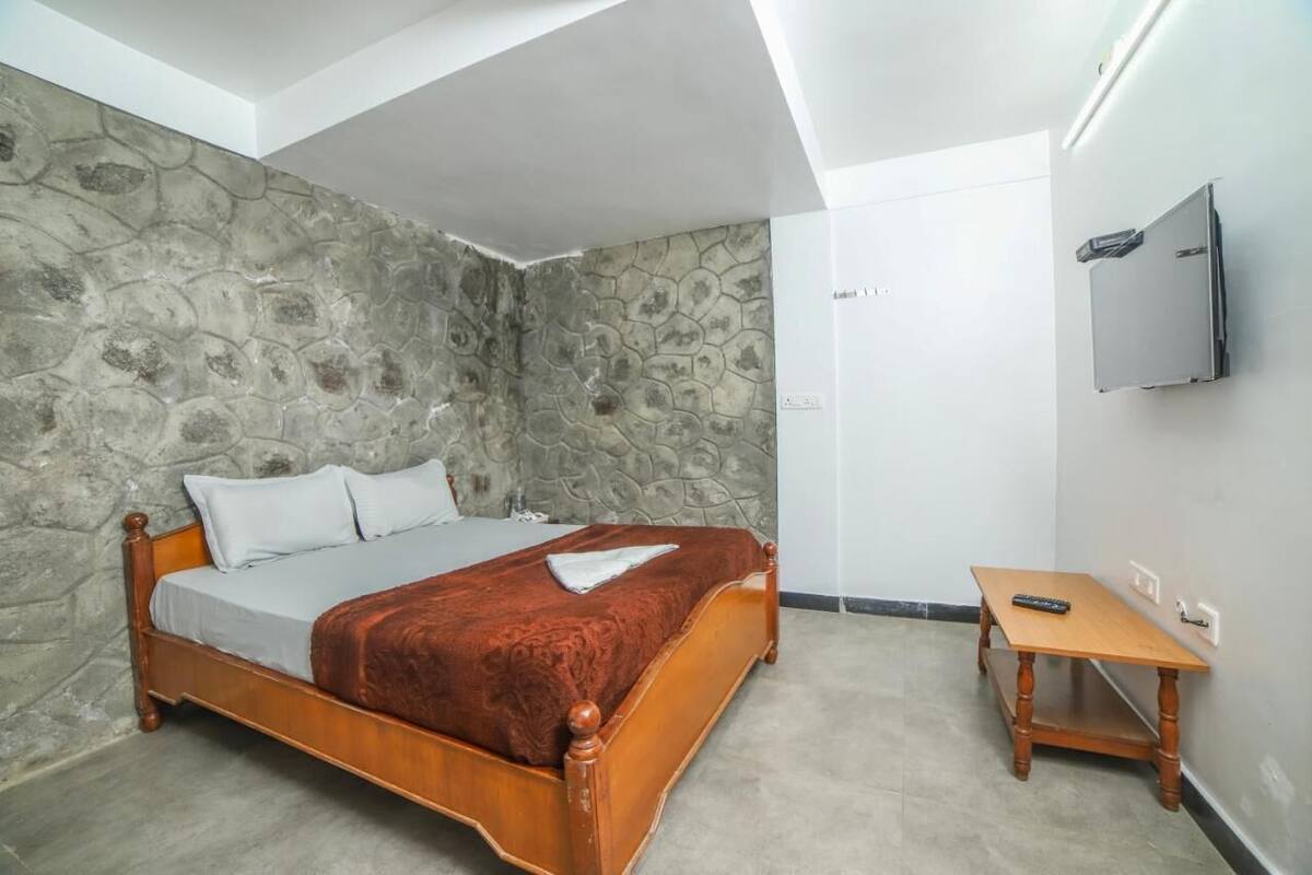 Ein Schlafzimmer mit Steinwand, einem hölzernen Bett, einem kleinen Holztisch und einem an der Wand montierten Fernseher.