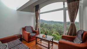 A room with two red sofas, a wooden coffee table, and a large window offering a view of a green landscape. - Peri Resorts by Indostays (Kotagiri)
