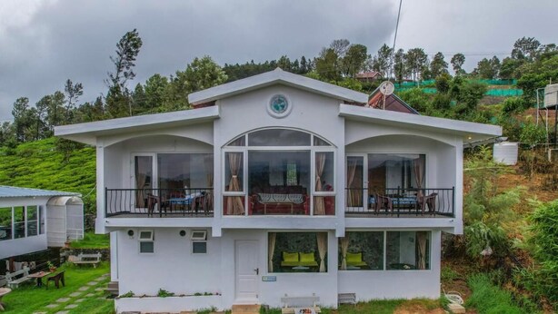 A two-story white building with a balcony on the upper floor, surrounded by greenery. - Peri Resorts by Indostays (Kotagiri)