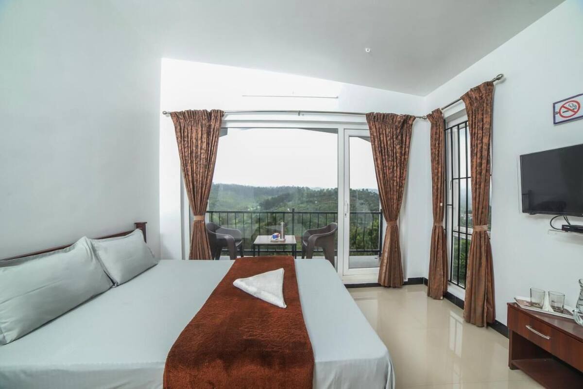 Ein Hotelzimmer mit Bett, Fernseher, einem Balkon mit Tisch und Stühlen sowie Vorhängen.