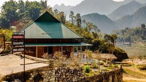 Une maison d’hôtes de style rustique, dotée d’un toit végétalisé, entourée d’une végétation luxuriante et de montagnes.