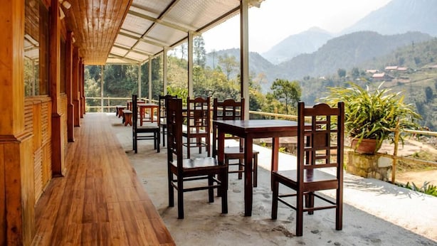 Un espace extérieur abrité, doté de tables et de chaises en bois, offrant une vue sur un paysage montagneux.