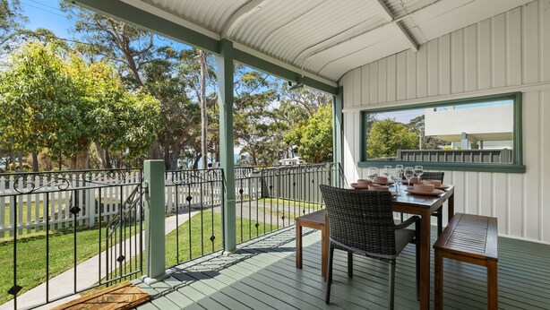 A covered outdoor area with a table set for dining, surrounded by a white fence and greenery. - The Gunyah by Experience Jervis Bay (Huskisson)