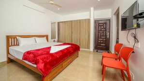 Un dormitorio con una cama de madera, una colcha roja, un ventilador de techo, un televisor montado en la pared y una puerta que da a otra habitación.