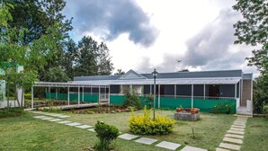 Un edificio moderno con un área exterior techada, un camino pavimentado y un pequeño jardín con arbustos y un árbol.
