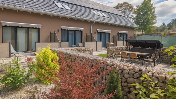 Un bâtiment doté d’un toit en pente, de grandes fenêtres et d’un patio aménagé avec du mobilier d’extérieur.