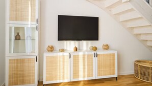 Un salon moderne avec un téléviseur fixé au mur, des meubles en osier blancs et un escalier en bois.