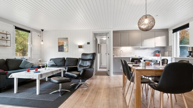 A modern living room with a sofa, a dining table, and chairs. There is a kitchen area with cabinets and a stove.