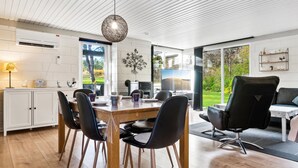 A modern kitchen with white cabinetry, a dining area with a wooden table and black chairs, and a large window offering a view of greenery.