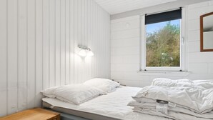A bedroom with a bed, a nightstand, a window, and a wall-mounted light fixture.