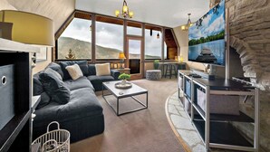 A modern living room with a large sectional sofa, a flat-screen TV, and a stone accent wall. - Ski-In/Ski-Out Schweitzer Chalet + Private Hot Tub - Guest Favorite (Sandpoint)