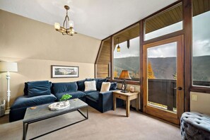 Una sala de estar acogedora con un sofá seccional, una mesita de centro y vistas a un paisaje montañoso a través de amplias ventanas.