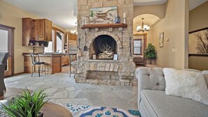 A stone fireplace with a mantel shelf, a kitchen with wooden cabinets, a dining area with a table and chairs, and a living room with a sofa and a potted plant. - Ski-In/Ski-Out Schweitzer Chalet + Private Hot Tub - Guest Favorite (Sandpoint)