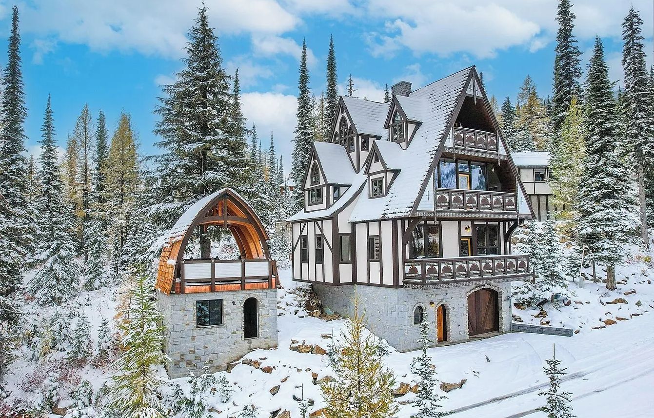 A chalet-style building with a steeply pitched roof, wooden beams, and a stone foundation, surrounded by snow-covered trees.