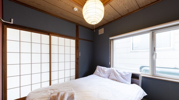 Une pièce comprenant un lit, des portes coulissantes de style shoji, une fenêtre et un luminaire suspendu.