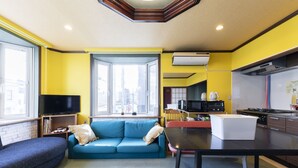 Un salon moderne avec un canapé bleu, un téléviseur à écran plat et un coin cuisine équipé d’un four à micro-ondes et d’une cuisinière.