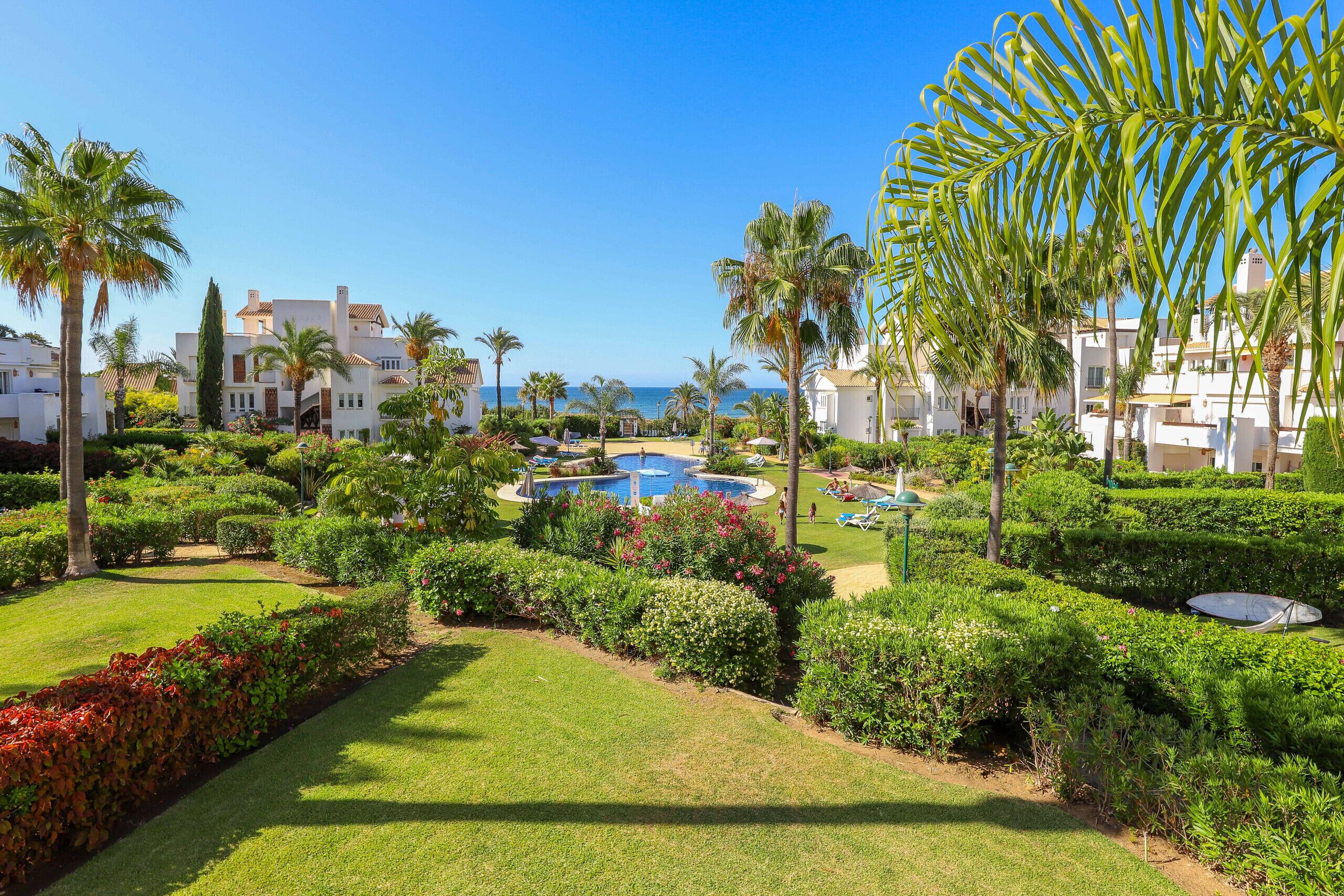 Een resort met een zwembad, palmbomen en uitzicht op zee.