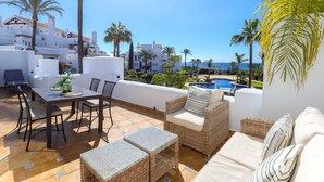 A terrace with a dining table, chairs, wicker furniture, and a view of a swimming pool and buildings. - Los Monteros Palm Beach - sea & pool views (Marbella)