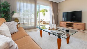 A modern living room with a glass coffee table, leather sofa, and a flat-screen TV on a wooden cabinet. - Los Monteros Palm Beach - sea & pool views (Marbella)
