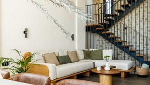 A modern living room with a white sofa, leather chairs, a coffee table, and a staircase with a metal railing. - Beach Villas in Crete Alope & Ava (Ierapetra)