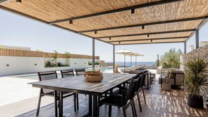 An outdoor patio with a wooden table and chairs, a pool, and a view of the sea. - Beach Villas in Crete Alope & Ava (Ierapetra)