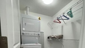 A laundry room with a stacked washer and dryer, a drying rack, and a trash bin. - Serene Haven in Harbour Landing (Regina)