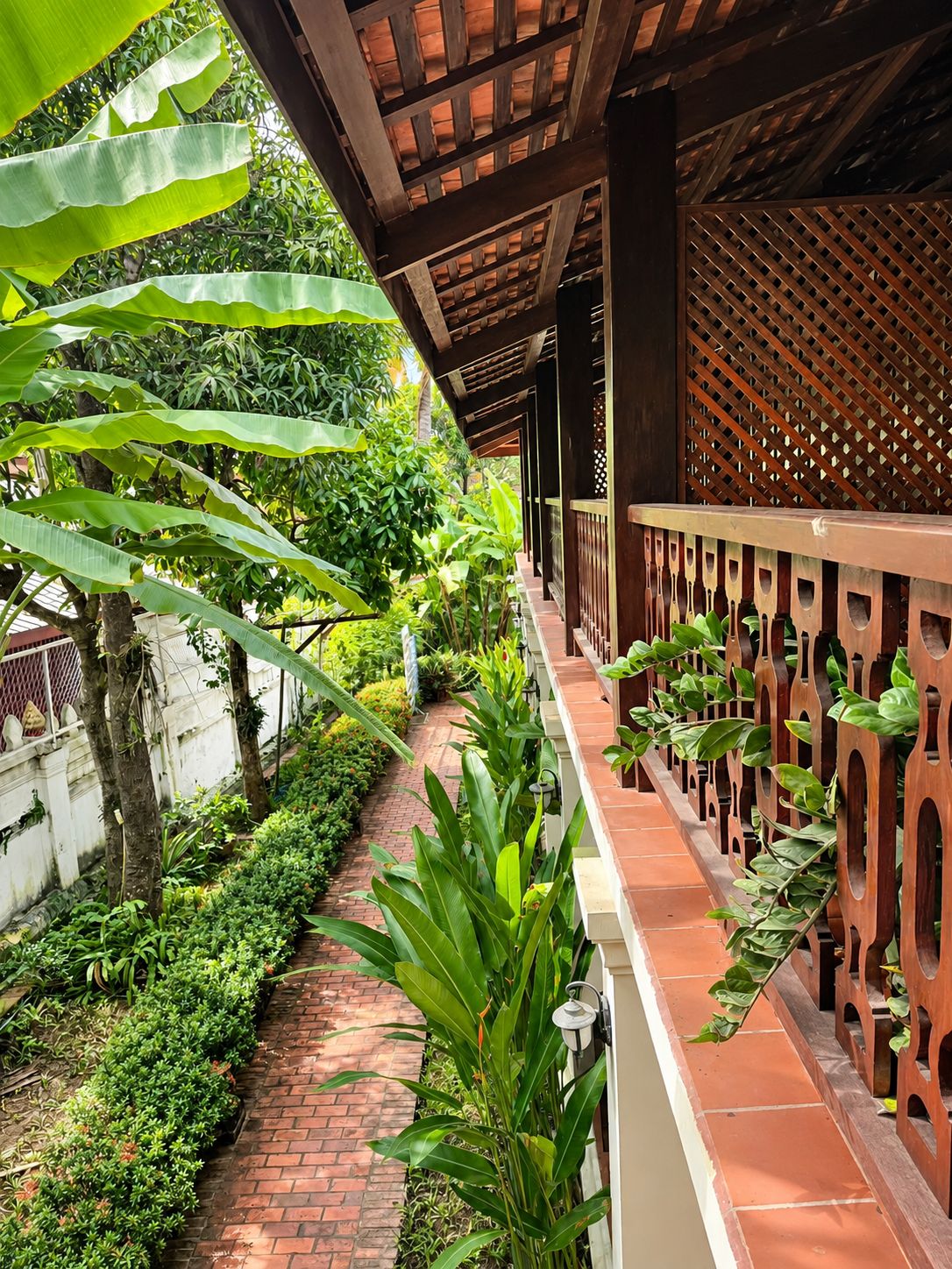 A covered outdoor area with a brick pathway, lush greenery, and a wooden lattice fence.
