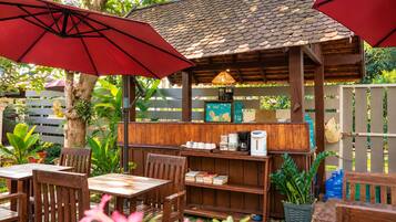 An outdoor café with wooden furniture, red umbrellas, and a coffee station.