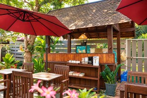An outdoor café with wooden furniture, red umbrellas, and a coffee station.