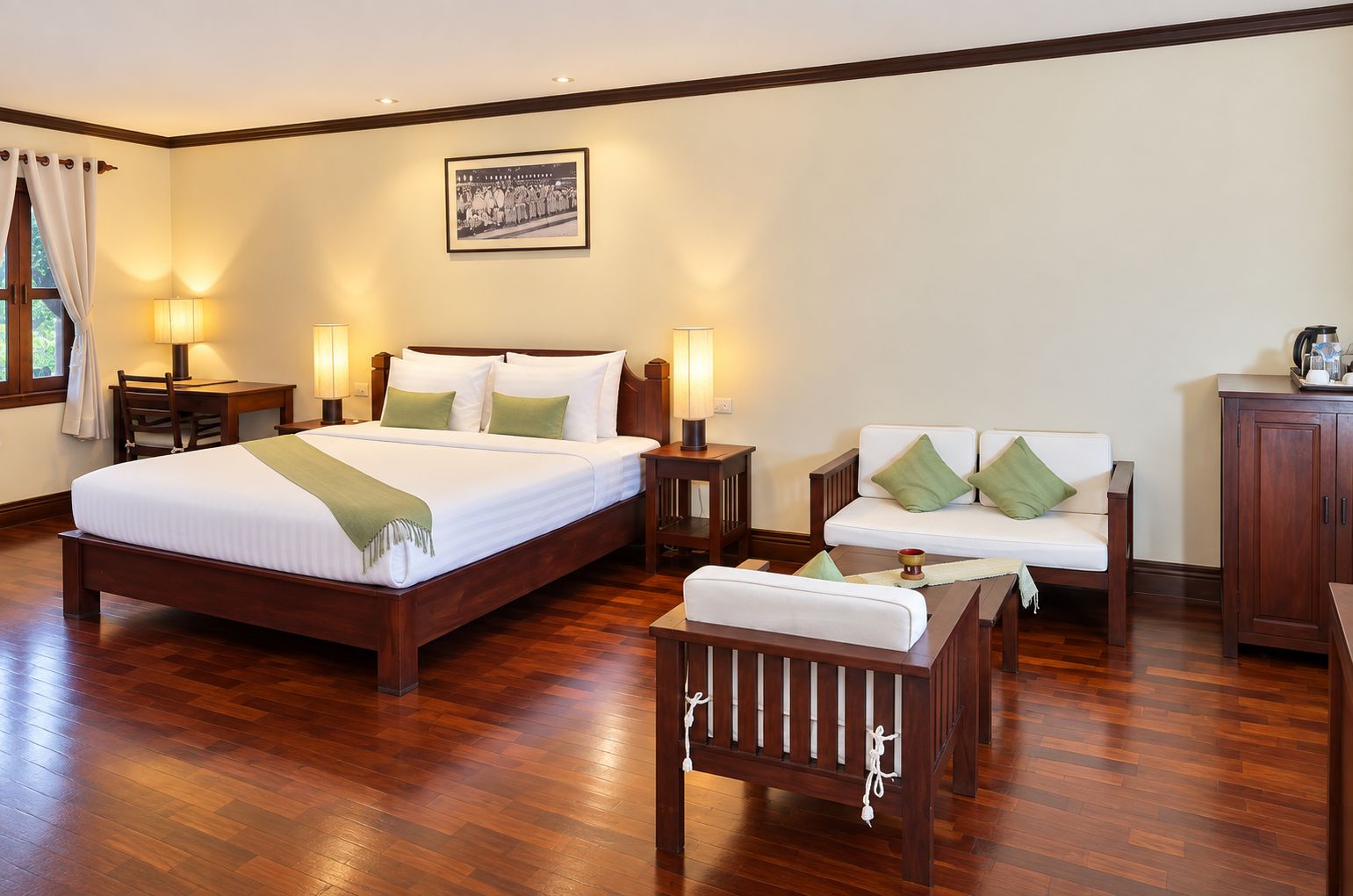 A hotel room with a large bed, a sofa, a chair, and a cabinet.