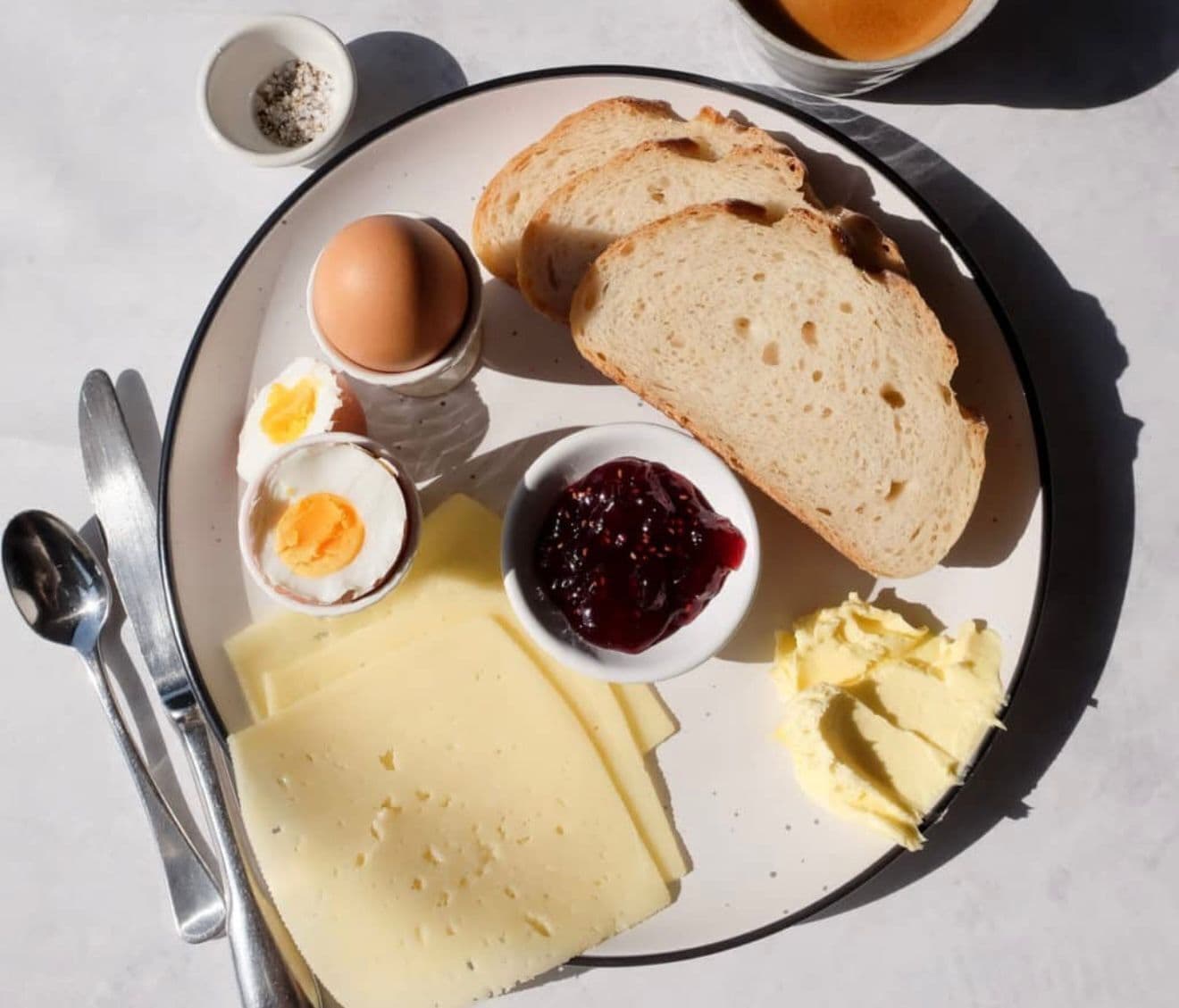 Un plato de desayuno con pan, huevos, queso, mantequilla y mermelada.