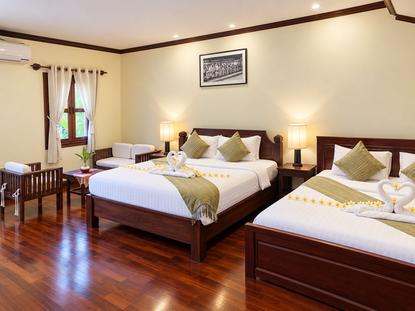 Habitació d'hotel amb dos llits, sòl de fusta, una finestra amb cortines, aire condicionat fixat a la paret i un quadre emmarcat.