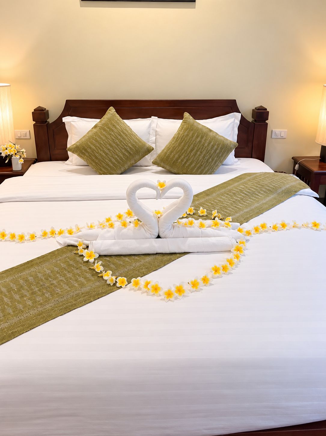 A hotel room with a neatly made bed, pillows, and a decorative heart-shaped towel arrangement.