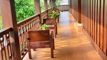 A covered outdoor area with wooden benches and a tiled floor, featuring a wooden railing and potted plants.
