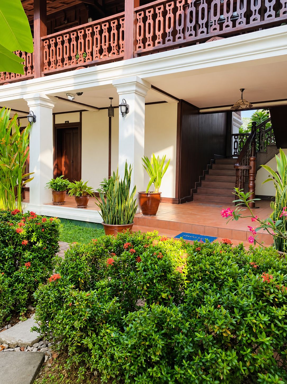Entrada de un hotel con porche cubierto, plantas en macetas y una escalera que conduce al interior.