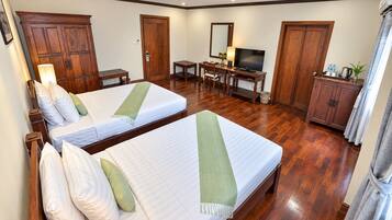 Habitación de hotel con dos camas, un escritorio con televisor y armarios de madera.