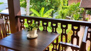 Una terraza de madera al aire libre con una mesa y sillas, rodeada de abundante vegetación y un suelo de baldosas.