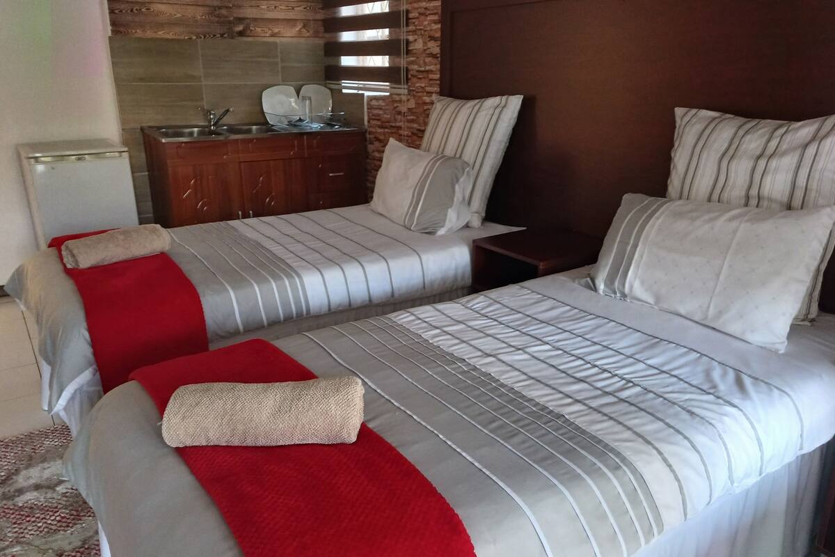 A hotel room with two beds, a wooden headboard, a small wooden cabinet, and a tiled backsplash.