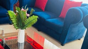 A living room with a glass coffee table, a blue sofa with red cushions, and a patterned carpet. - Comrades Oasis Guest House  (Pietermaritzburg)