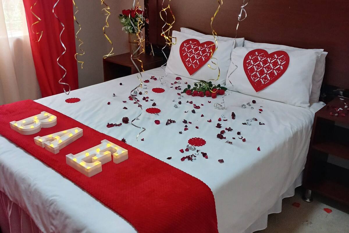 A bed with a white and red bedspread, two heart-shaped pillows, and a 'LOVE' sign on the bed.