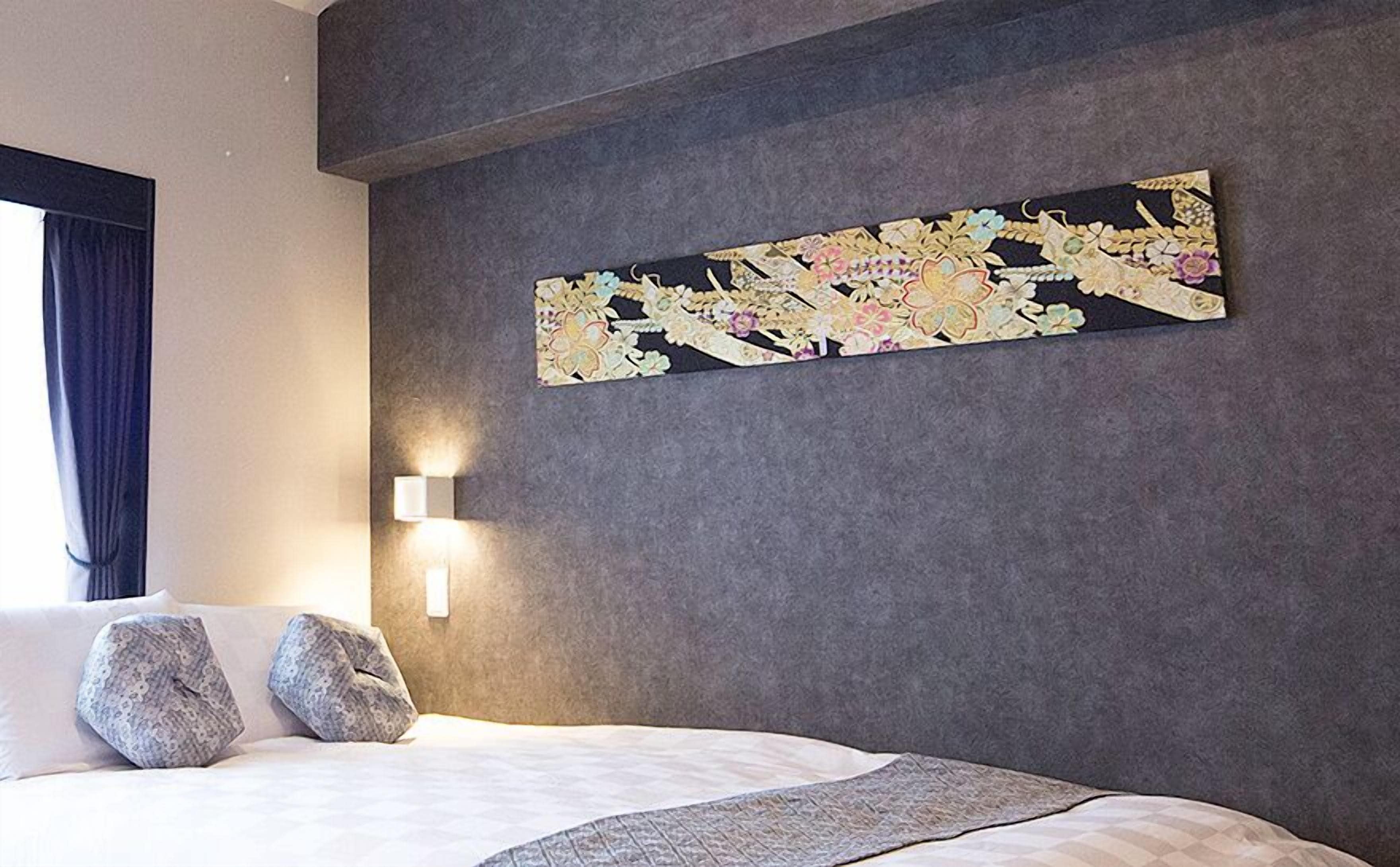 A hotel room with a large bed, two pillows, a textured wall, and a decorative wall hanging.