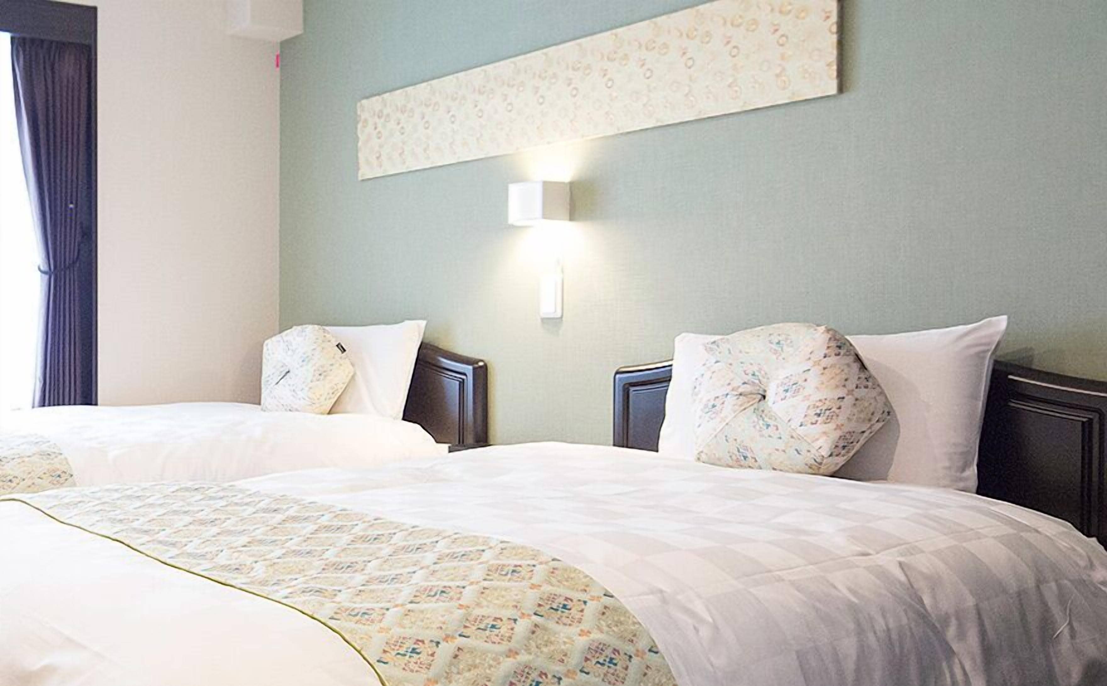 A hotel room with two beds, each with a patterned pillow and a quilted bedspread.
